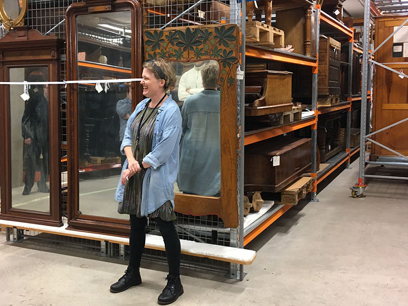 Annelie står i ett magasin med museiföremål bakom sig. Foto.